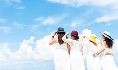 Group of four women in white dress and wearing hat standing along the beach with blue sky background. Summer and vacation conceept.