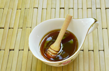 wooden honey scoop in cup on bamboo plate