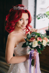 young beautiful bride holding a bouquet and standing near the window in the loft