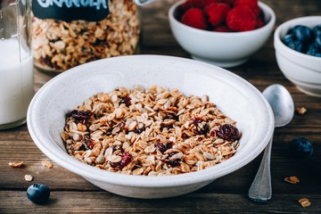 Homemade granola cereal with oats and nuts and dry cranberries. Healthy breakfast with milk and berries.
