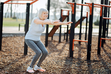 Vigor. Cheerful aged woman doing squats and exercising in the open air