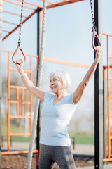 Cheerfulness. Glad blond woman doing chin-ups while exercising in the open air