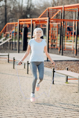 Favourite exercise. Alert thin woman jumping rope while exercising in the open air
