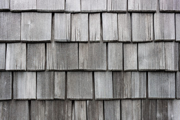 Wood shingle wall siding made of larch. Old, discolored and worn by weather shingles. Traditional austrian house siding.