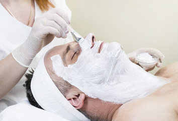 A man does the procedure cleaning his face with a clay mask in the beauty salon 