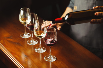 Bartender pours red wine in glasses on wooden bar counter