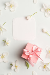 pink gift and white card surrounded by Apple flowers. pretty background top view, copy space. love message, congratulations on mother's day, spring, Valentine's day, women's day