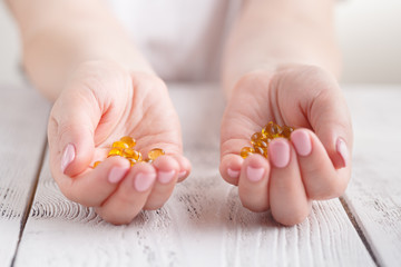 healthy eating, medicine, health care, food supplements and people concept - close up of woman hands holding pills or fish oil capsules at home