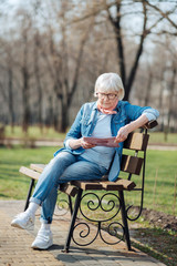 Recreational. Determined blond woman reading a magazine while sitting on the bench