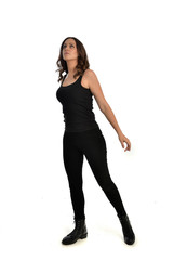 Fototapeta premium full length portrait of brunette girl wearing black singlet, jeans jeans and boots. standing pose, isolated on white studio background.