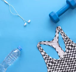 Tuinposter sports top, blue dumbbell, headphones, water bottle on blue background,  flat lay © Elena