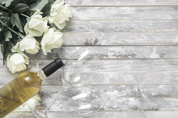 White roses and a bottle of white wine and two wine glasses on a wooden gray vintage table. Valentine's Day, 8 March, wedding, birthday. Flat lay, top view, copy space 