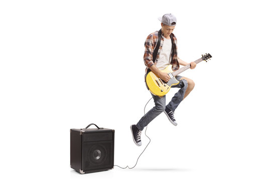 Teenage boy with an electric guitar plugged in an amplifier jumping