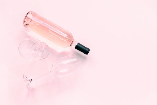 Bottle of pink wine and two glasses of wine on a soft light pink wood table, mock up. Flat lay, top view, copy space 