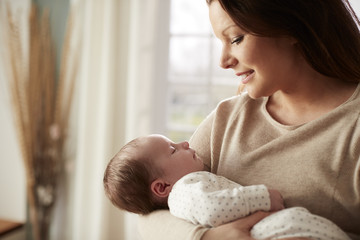 Loving Mother Cuddling Newborn Baby At Home