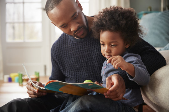 Father And Young Son Reading Book Together At Home