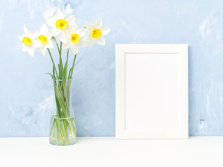 Bouquet of fresh flowers, white frame on table, opposite blue textured concrete wall. Empty space for text. Mock up.