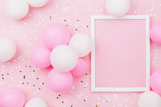Birthday mockup with frame, pastel balloons and confetti on pink table top view. Flat lay composition.