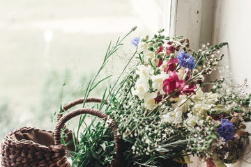 wildflowers in wicker bag on rustic white window. colorful flowers in brown basket in sunlight,...