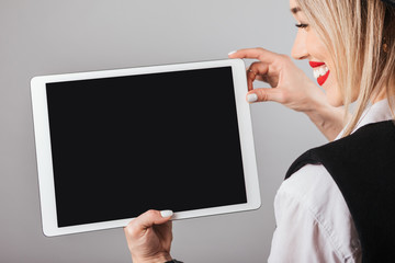 Blonde woman showing empty screen tablet computer. Gray background. You can place your text information, image or logo
