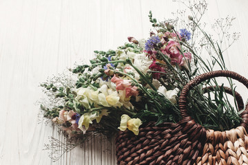 beautiful wildflowers in wicker bag on rustic white wooden background flat lay. colorful flowers in basket in light, space for text, top view. rural atmospheric moment. summer picture