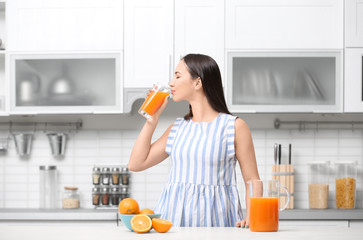 Young woman drinking orange juice in kitchen