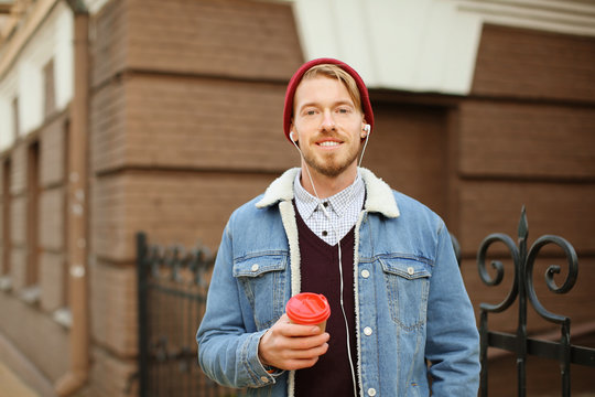 Portrait of hipster with earphones listening to music and drinking coffee outdoors