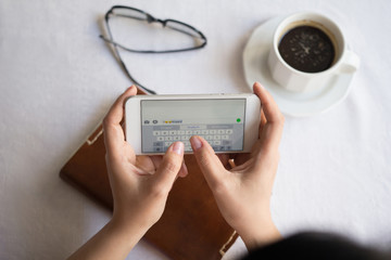 Up view image of woman hands typing message on modern phone. Cup of coffee next to her.