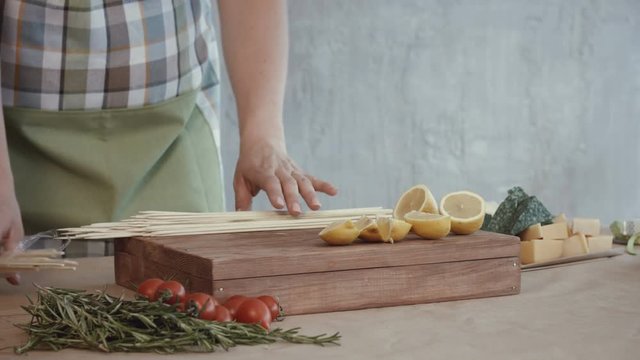 Closeup of female hands pinning slices of fresh lemon on wooden skewers while making edible arrangement in the kitchen. Midsecton of woman in apron pinning pieces of lemon on skewers.