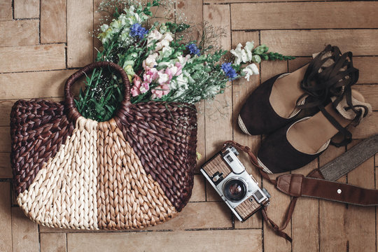 beautiful wildflowers in wicker bag and film camera and hipster woman shoes on rustic wooden background top view. flowers in basket and girl sandals, space for text. rustic fashion