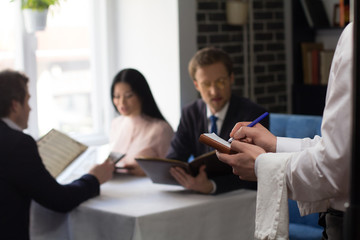 Business partners choosing dishes from menu at luxury restaurant. Waiter taking order.