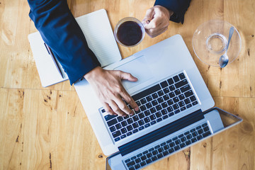 Top view of one businessman hand working on laptop computer and another hand holding a cup of black coffee