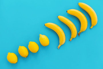 summer flat lay. yellow bananas with lemons in line on blue paper trendy background, flat lay. bright colorful photo, with space for text. juicy abstract background, pop art style