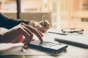 Close up hands businessman doing finances with using calculator and writing note in office.