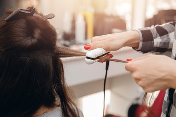 Hairdresser woman straightens her hair and makes styling, close-up of curling iron in salon