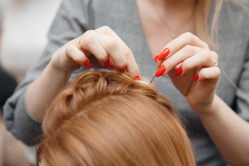 Hairdresser does hairstyle for woman to weave braids, styling. Concept wedding specialist,...