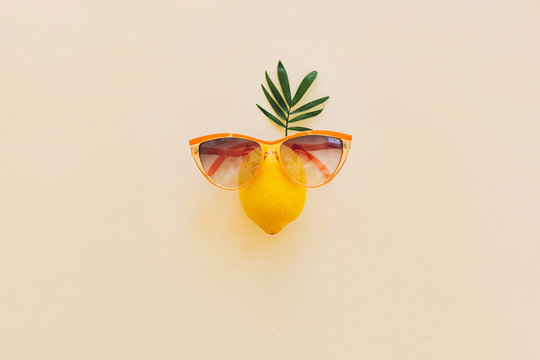lemon in stylish sunglases with palm leaf on pastel yellow paper trendy background, vacation flat lay. modern summer flat lay concept, with space for text. funny and juicy abstract