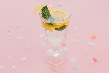 fresh cocktail with lemon and mint in vintage glass on trendy pink paper background with confetti. mojito. summer vacation and party concept, colorful pattern. refreshing drinks.