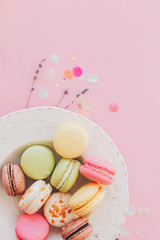 delicious colorful macaroons in vintage white plate on trendy pastel pink paper, stylish flat lay. tasty pink, yellow, green and brown macarons with lavender and confetti. space for text