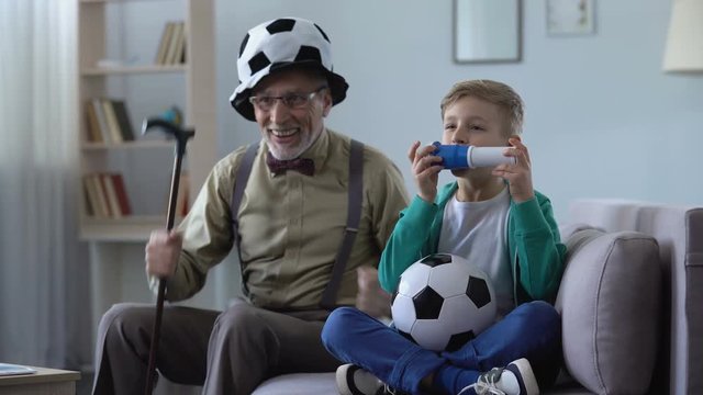 Grandpa in crazy football hat and boy cheering for national team with fan horn