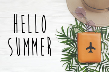 Hello Summer text on passport with plane and retro black sunglasses,hat, green palm leaves on white wooden background. stylish summer vacation flat lay. hello holidays