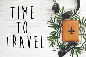 Time to Travel text on passport with plane, retro black sunglasses and headphones on green palm leaves on white wooden background. modern travel and vacation flat lay