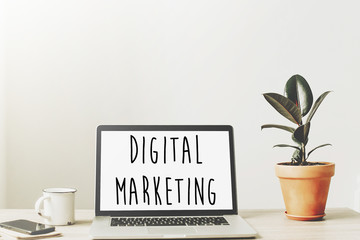 digital marketing text on laptop screen on wooden desktop with phone, notebook, coffee and plant. business workspace. business analysis and strategy