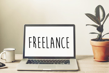 Freelance text on laptop screen on wooden desktop with phone, notebook, coffee and plant. space for...