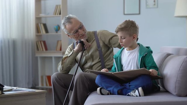 Boy reading book aloud, happy grandfather listening, stroking grandson head