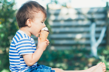 a child in a t-shirt on a bench eating ice cream in the summer is very greedy