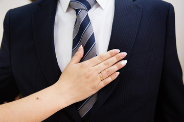 Wedding boutonniere on suit of groom and bride’s hand 