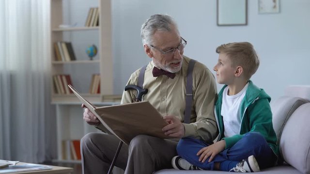 Kind old man reading fairy tale to grandson, docile boy leaning against shoulder