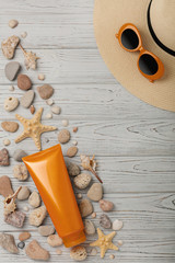 Suntan cream on a gray wooden background, hat, sunglasses and shells, sea stones and a starfish.