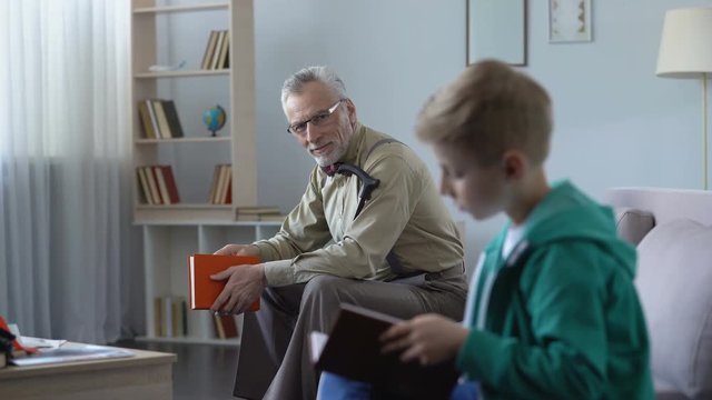 Little boy reading paper book, his grandfather watching with proud, education